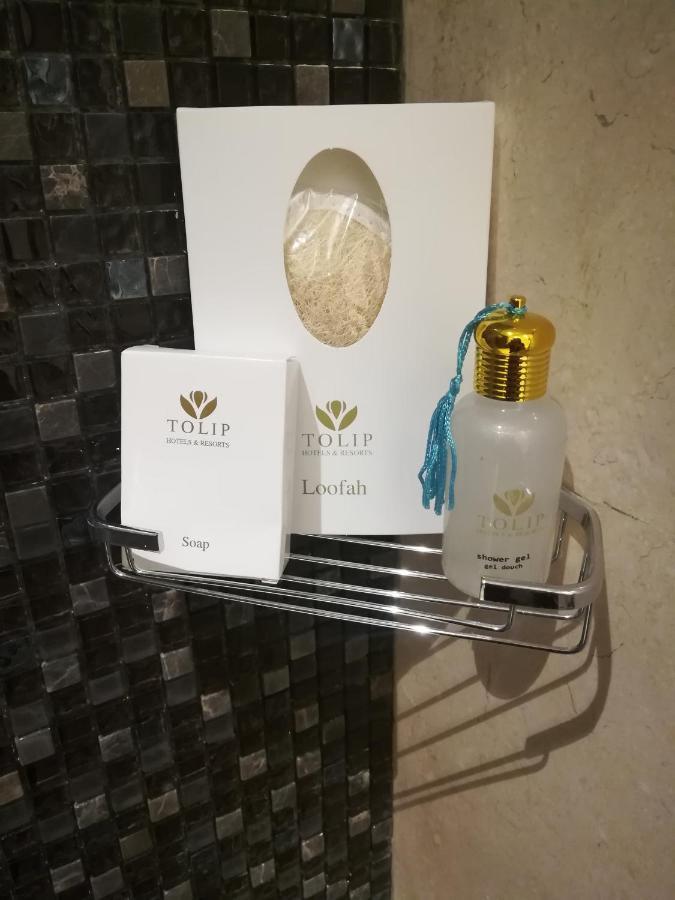 Tolip Resort El Galala Majestic Αΐν Σούχνα Εξωτερικό φωτογραφία The photo shows a small metal shelf containing three items related to personal care. 

1. **Soap**: A white box labeled "TOLIP" with the word "Soap" visible on the front.
2. **Loofah**: A package with the same "TOLIP" branding, containing loofah.
3. 